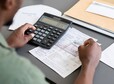 Close-up of unrecognizable blackman sitting at table and checking bills while calculating personal finances