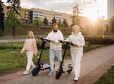 A family in white clothes walks around the city with electric scooters at sunset.Outdoor activities.